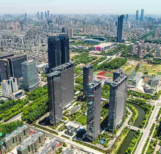 Aerial view of a cityscape with numerous high-rise buildings, green spaces, and a river running through the urban area under a clear sky.