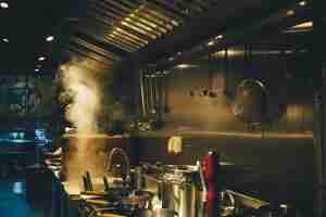 A commercial kitchen with pots, pans, and utensils hanging on a metallic wall; steam is rising from a large pot on the stove under bright overhead lights.