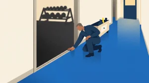 A person in a blue uniform kneels on a blue floor, inspecting the base of a glass wall. Behind the glass, there is a rack of exercise weights casting a shadow. A janitorial cart sits in the hallway nearby.
